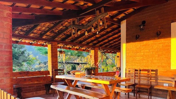 An outdoor patio with wooden tables and benches, brick walls, and hanging lights.