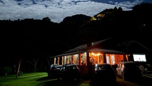 A building with a porch, cars parked in front, and a night sky with clouds and a visible moon.