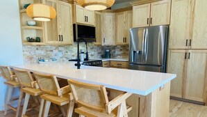 Una cocina moderna con armarios de madera, una isla grande con taburetes de bar y electrodomésticos de acero inoxidable.
