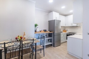 A modern kitchen with white cabinets, a stainless steel refrigerator, and a dining area with a table and chairs.
