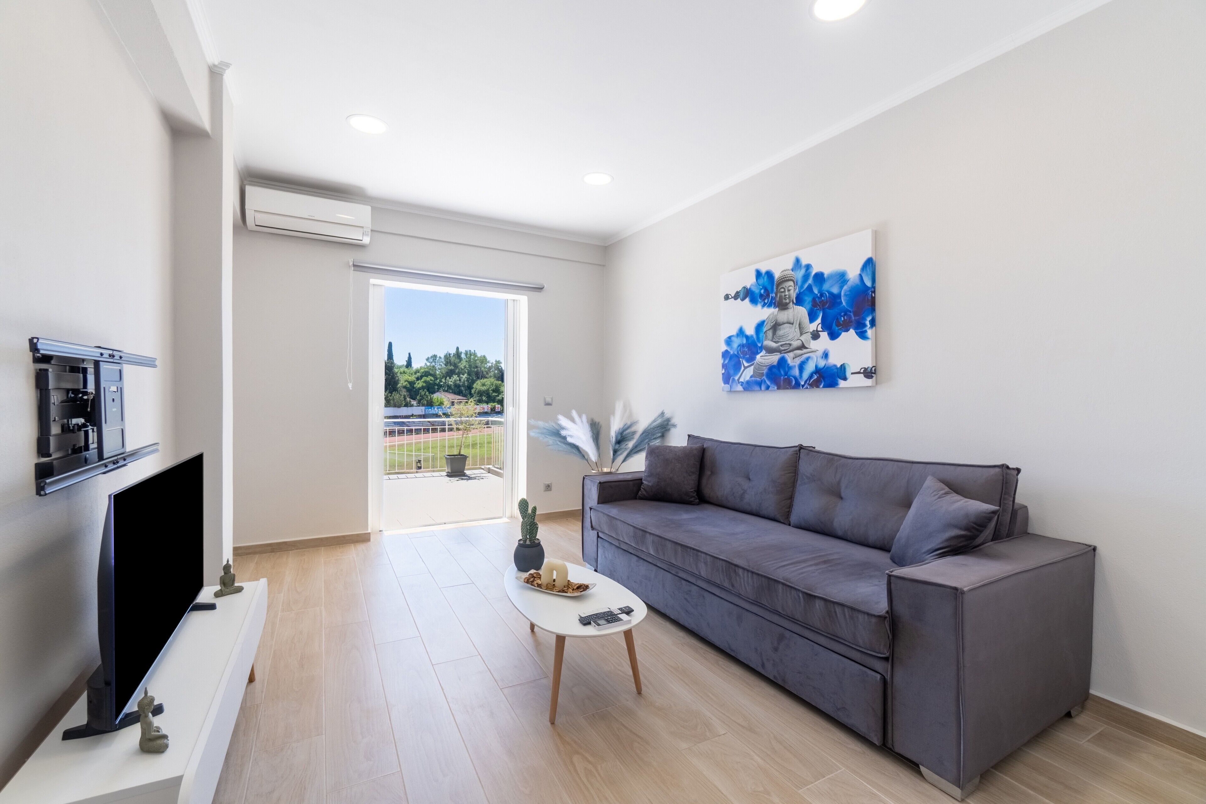 Uma sala de estar moderna com um sofá cinzento, uma televisão de tela plana, uma mesa de centro branca e um quadro na parede.