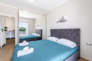A modern hotel room with a large bed, a mirror, a small desk, and a view of the outdoors.