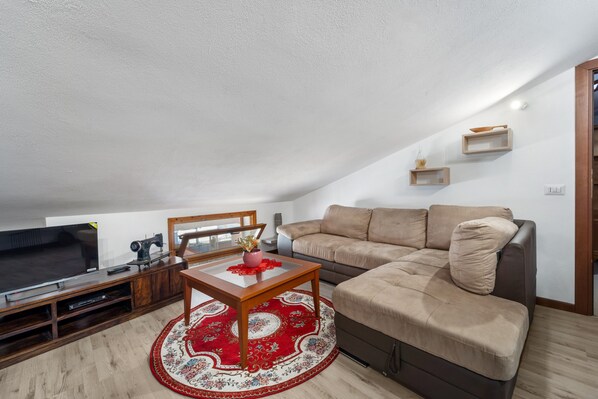 Una sala de estar moderna con un televisor de pantalla plana grande, una mesa de centro de madera, un sofá modular beige y un tapete rojo estampado.