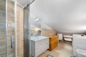 Un baño moderno con ducha de vidrio, lavamanos blanco, armarios de madera y lavadora integrada.