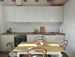 Une cuisine avec des meubles blancs, un plan de travail en bois, un évier, une planche à découper et un saladier rempli de fruits.