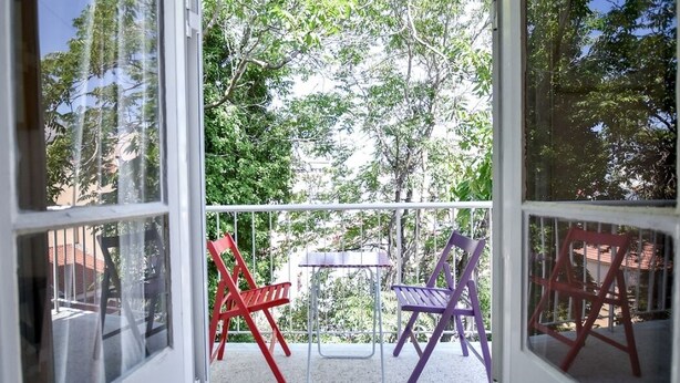 Een balkon met een tafel en twee stoelen, omgeven door een witte balustrade en bomen.