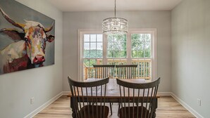 Un coin repas avec une table et des chaises en bois, un lustre et un grand tableau représentant une vache accroché au mur.