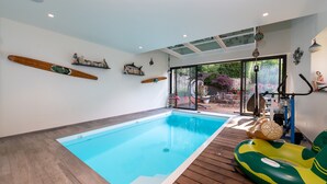 Une piscine intérieure avec un plancher en bois, une porte vitrée donnant sur l’extérieur et un flotteur gonflable vert.