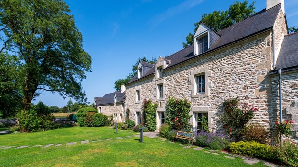 Un bâtiment en pierre doté de nombreuses fenêtres et d’un jardin bien entretenu.