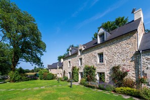 Un bâtiment en pierre doté de nombreuses fenêtres et d’un jardin bien entretenu.