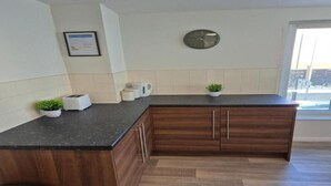 A modern kitchen with a dark countertop, wooden cabinets, a clock, and a small plant. - Sandard Room In Town Centre (Middlesbrough)