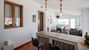 Una cocina moderna con una isla central, paredes de azulejos blancos y una zona de comedor con sofá y sillas.