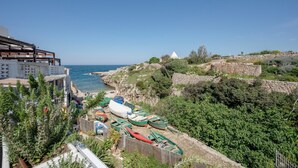 Vista costera con barcos, un muro de piedra y un edificio con techo inclinado.