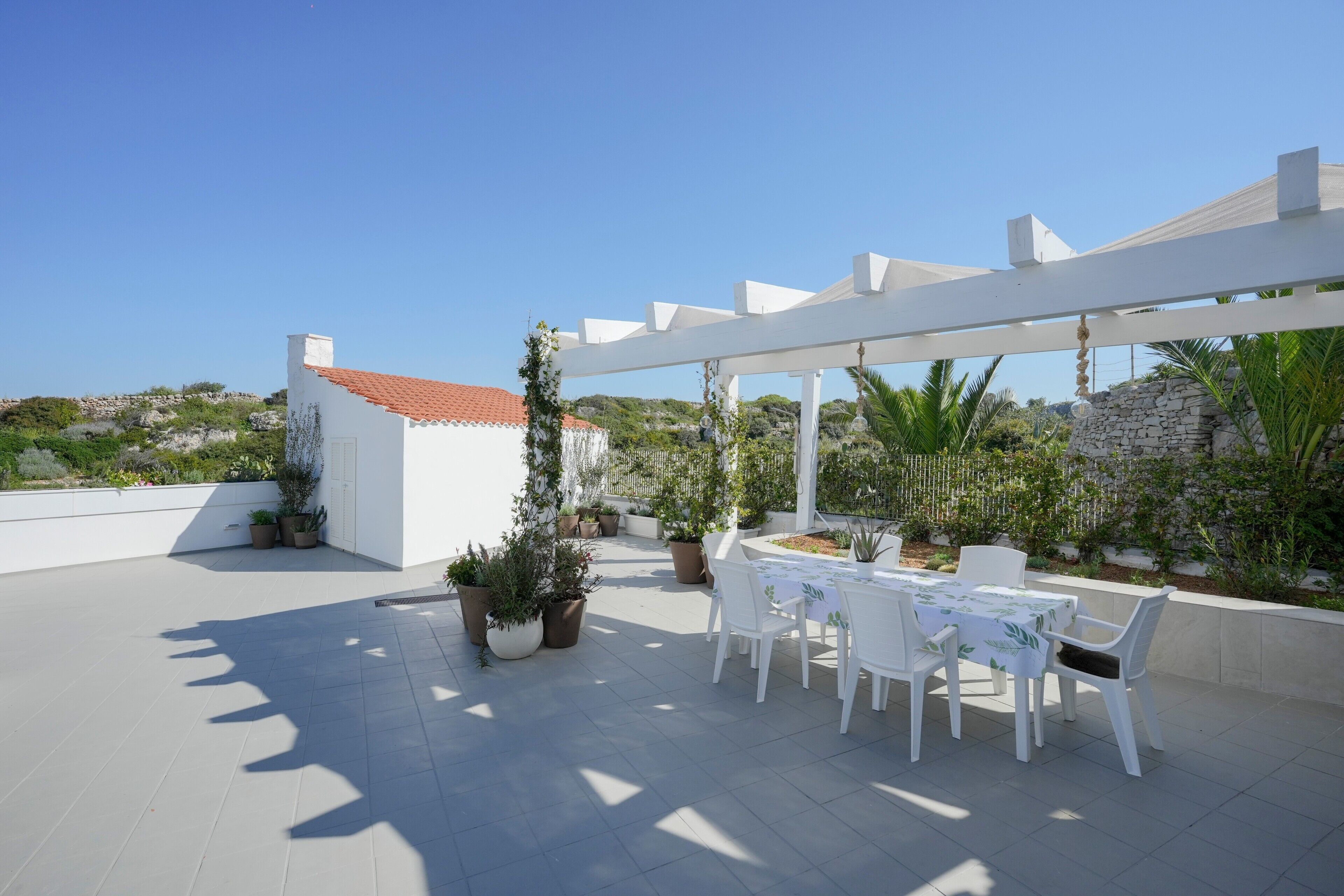 A rooftop patio with a table and chairs, potted plants, and a white pergola.