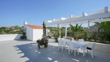 A rooftop patio with a table and chairs, potted plants, and a white pergola.