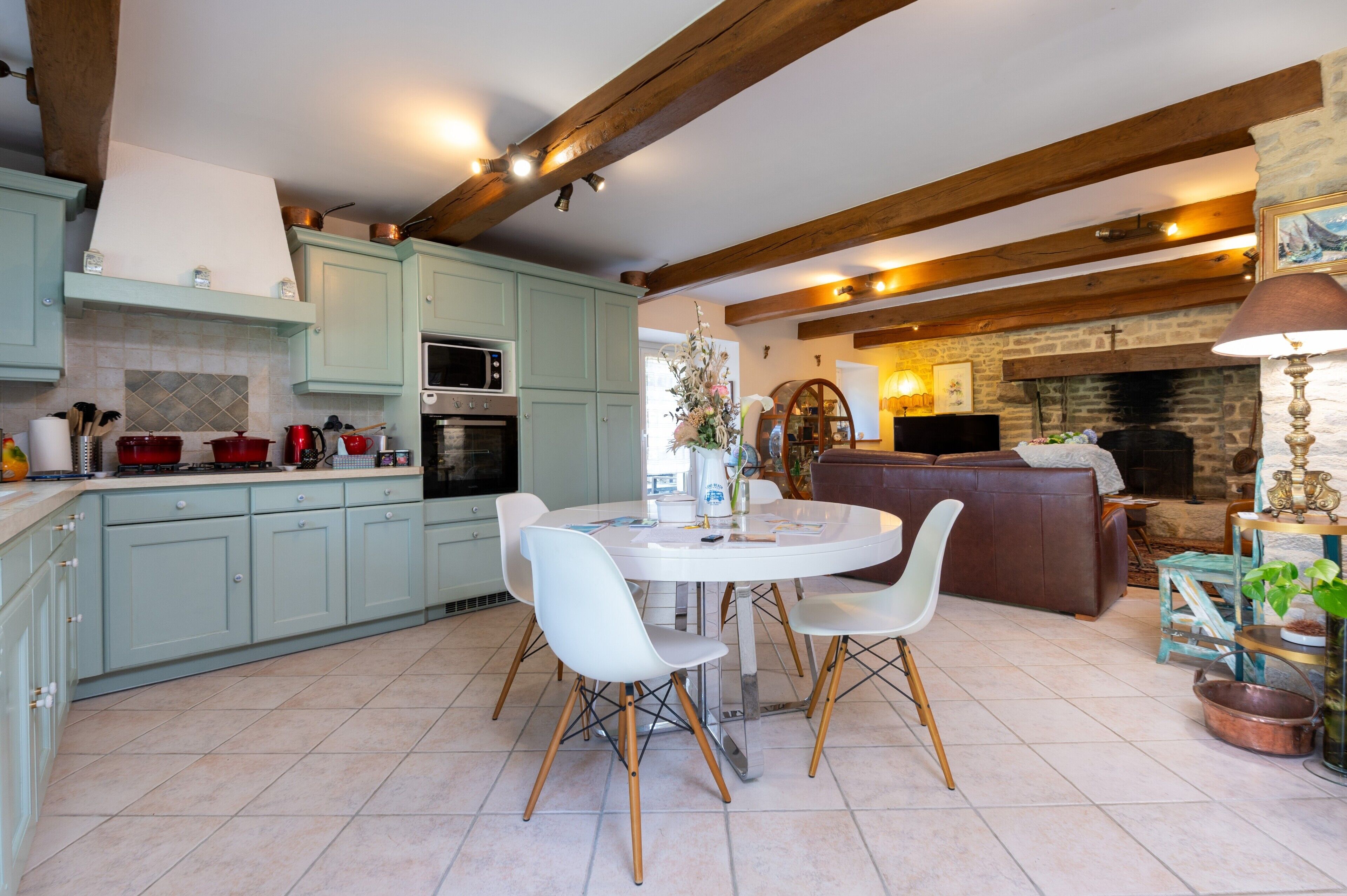 Una cocina con alacenas azul claro, una mesa de comedor con sillas, una chimenea y un televisor.