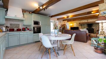 Una cocina con alacenas azul claro, una mesa de comedor con sillas, una chimenea y un televisor.