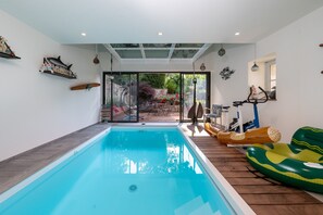 An indoor swimming pool with a wooden deck, a slide, and a view of a garden.
