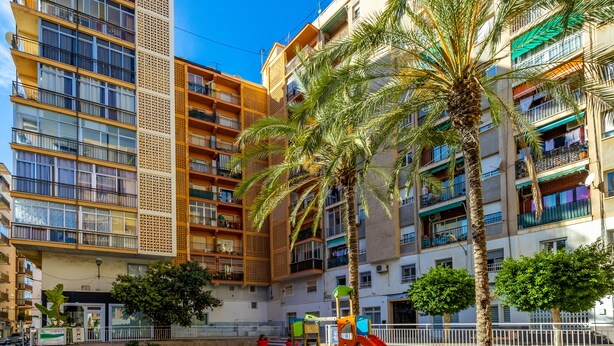 A multi-story residential building with balconies, a playground with a slide, and palm trees. - Inftour Garvimar Apartamento (Calp)