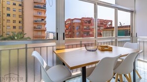 A balcony with a wooden table, white chairs, and a wicker basket. - Inftour Garvimar Apartamento (Calp)