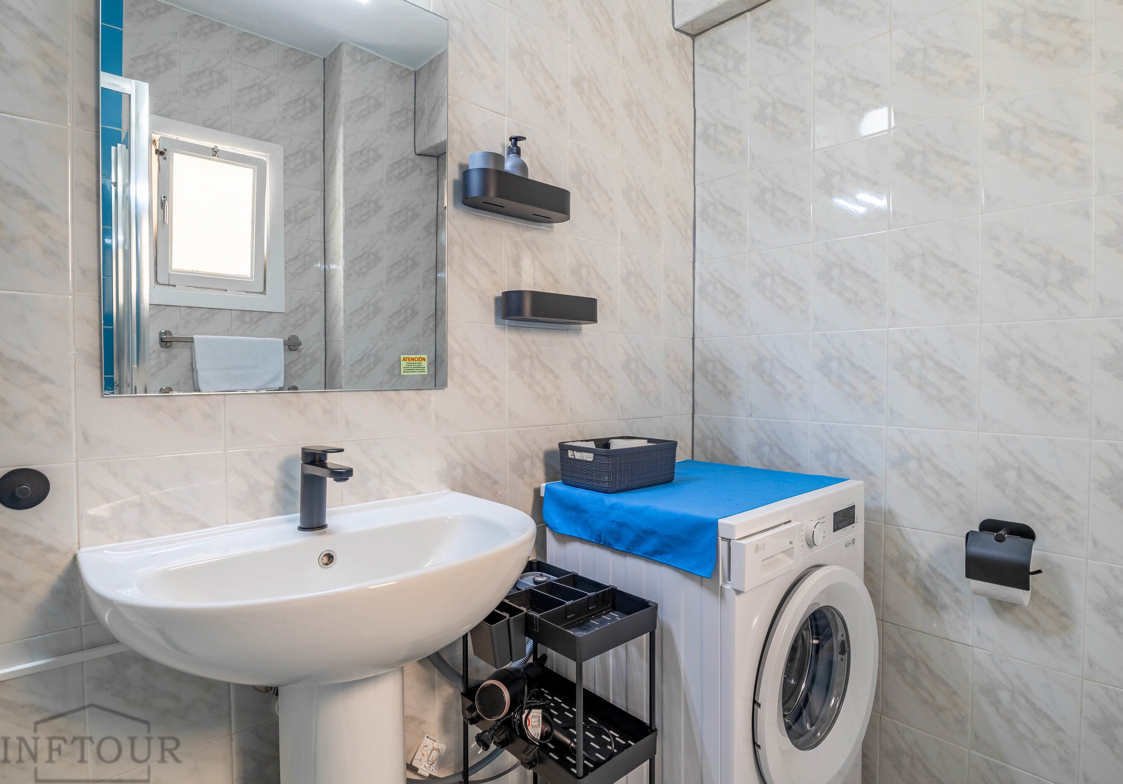 A bathroom with a sink, mirror, towel rack, and a washing machine.