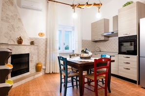 A kitchen with a stone wall, a fireplace, a dining table with chairs, and modern appliances.