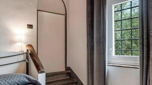Une chambre à coucher comprenant un lit, une table de chevet, une lampe, une tête de lit en bois, une fenêtre avec des rideaux et un escalier.