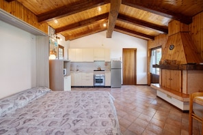 Un dormitorio con cama, una cocina con armarios, un refrigerador y techo de madera.