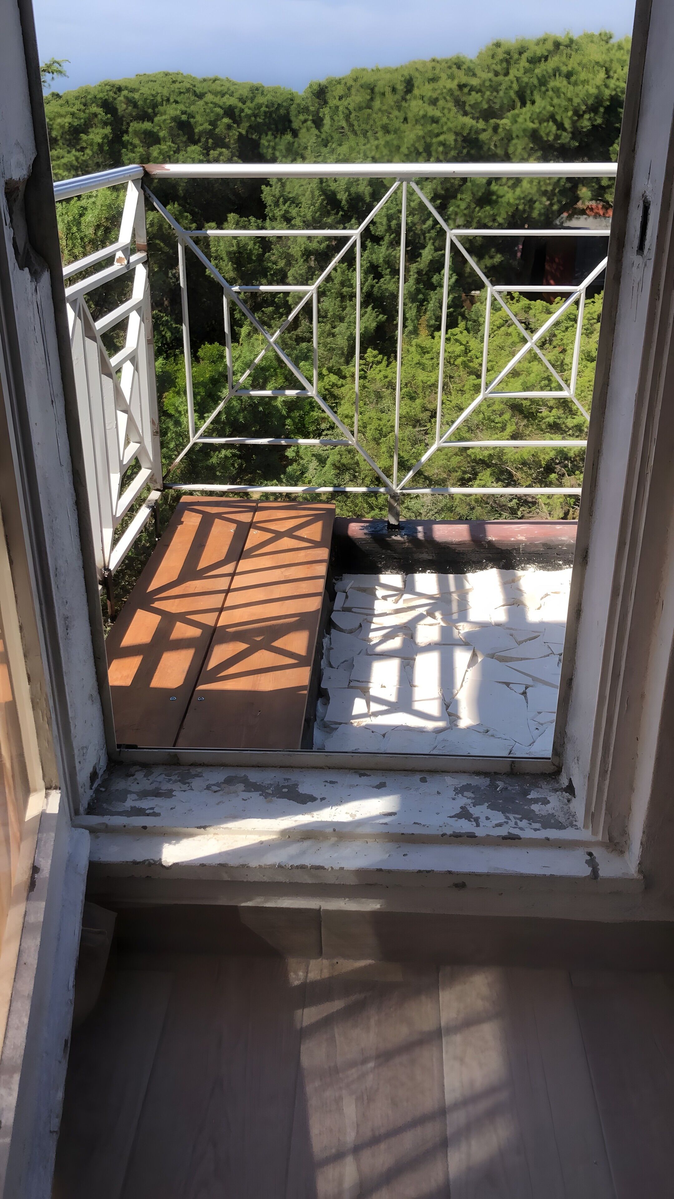 Ein Balkon mit Metallgeländer, Holzboden und Blick auf einen grünen Wald.
