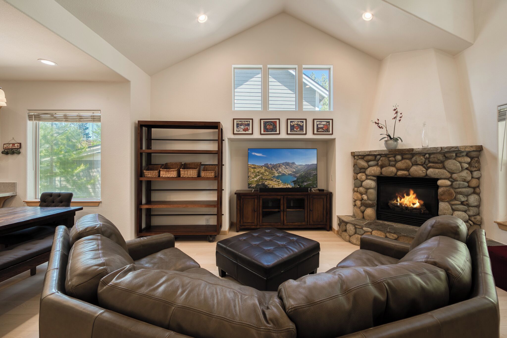 Una sala de estar con chimenea de piedra, sofás de cuero, televisor y estantería.