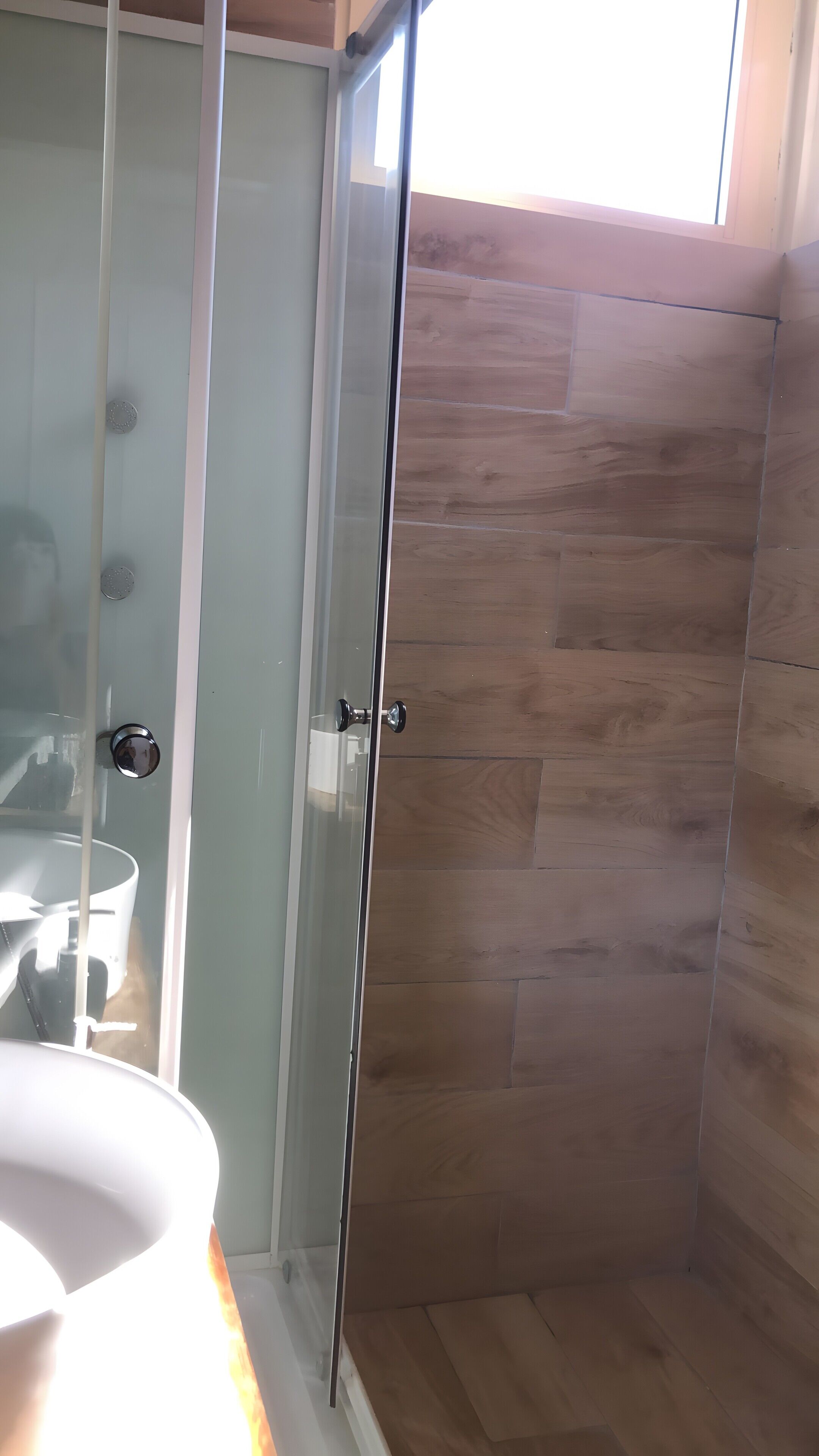 Un bagno con box doccia in vetro, lavandino bianco e pavimento in legno.