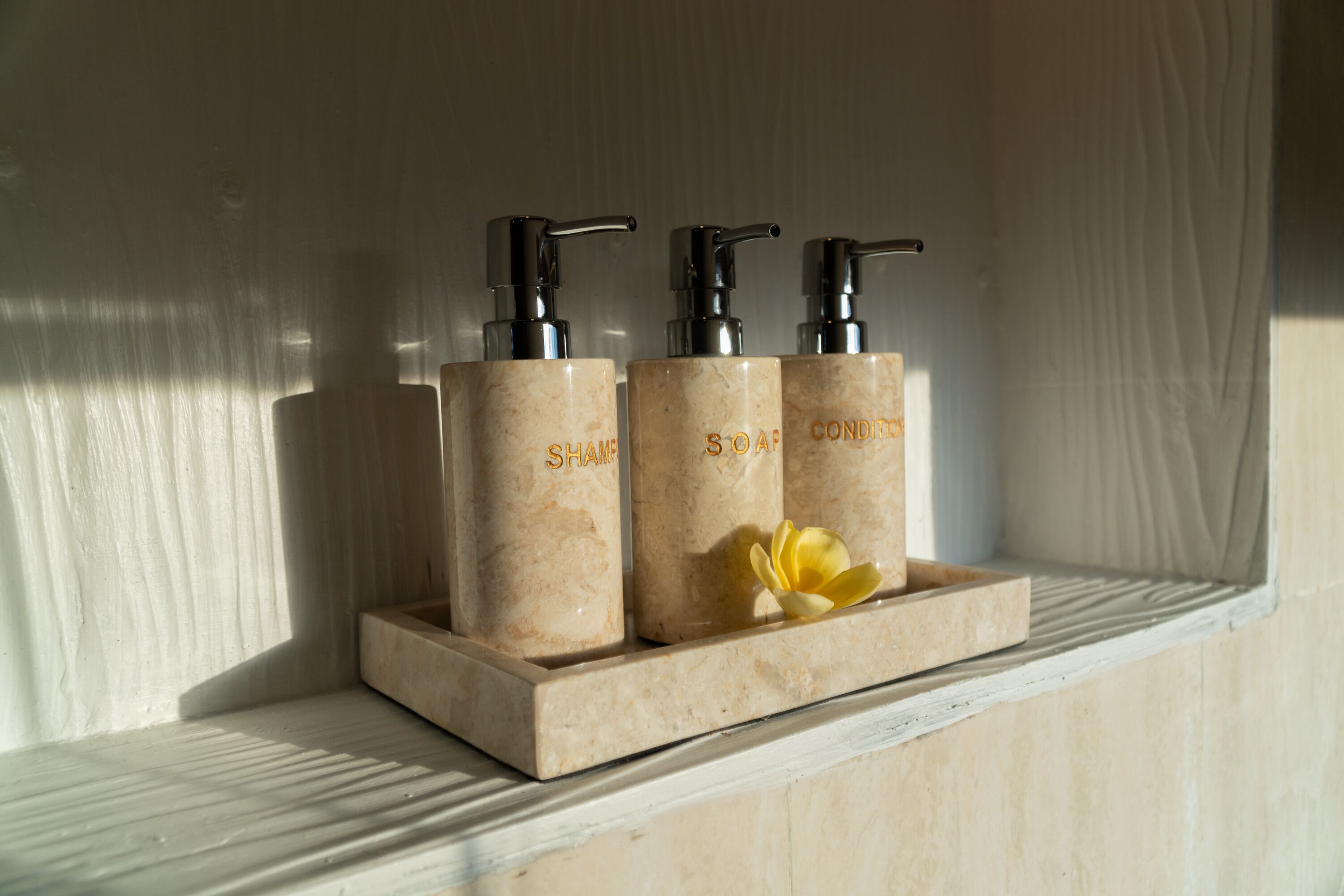 Three bottles of shampoo, soap, and conditioner on a marble shelf.