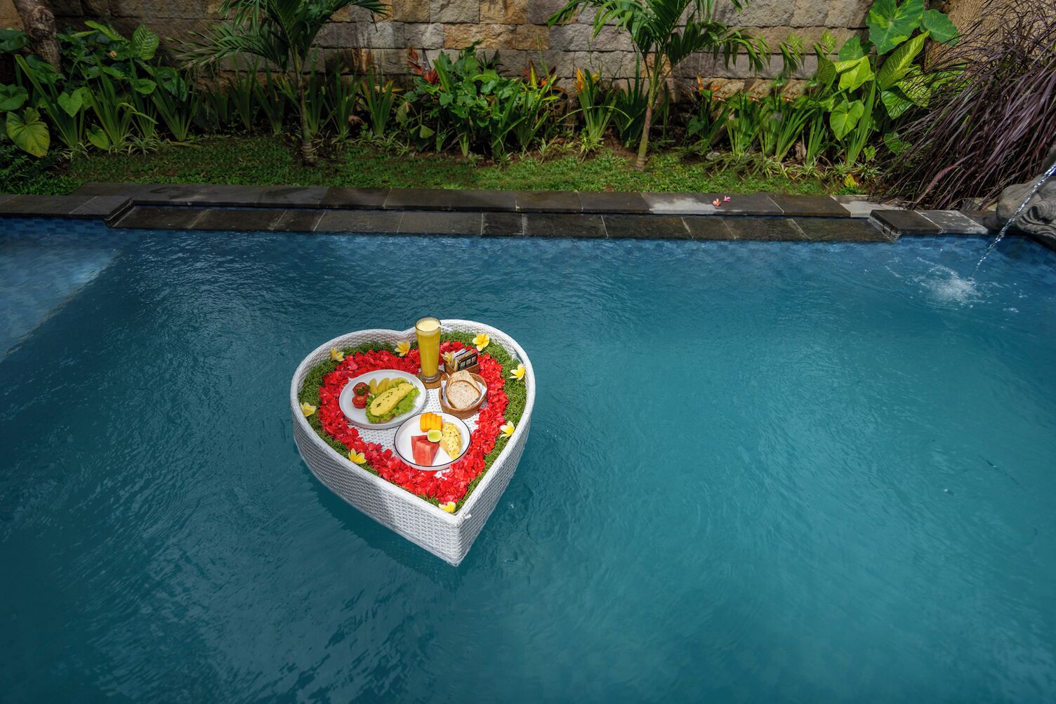 A heart-shaped floating platform with food and drinks in a pool.