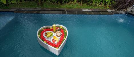 A heart-shaped floating platform with food and drinks in a pool.