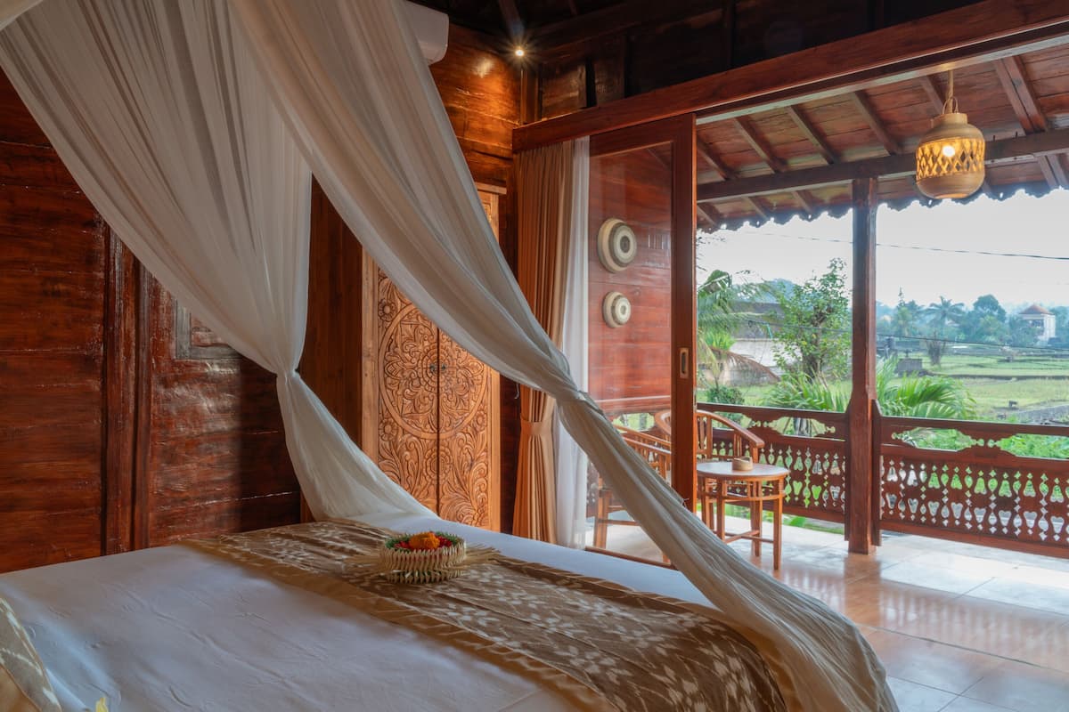 A bedroom with a bed, a canopy, a view of the outdoors, and a balcony with a table and chairs.