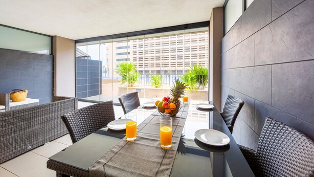 A dining area with a table set for two, a fruit bowl, and two glasses of orange juice.