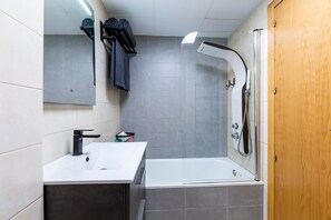 Une salle de bain avec un lavabo blanc, une baignoire, une douche, une porte en bois et un miroir.