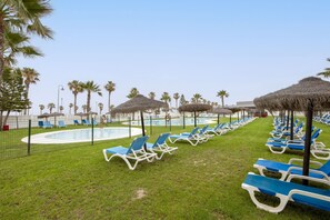 Un espace piscine agrémenté de chaises longues et de parasols, entouré de palmiers.