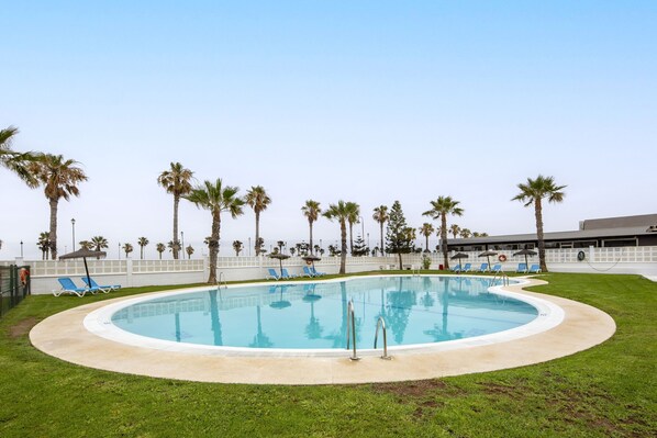 Une piscine avec des chaises longues bleues, des palmiers et un bâtiment en arrière-plan.