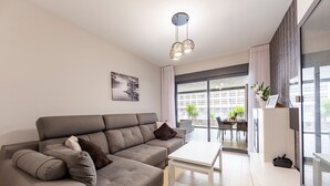 A modern living room with a grey sectional sofa, a white coffee table, and a large window with a city view.
