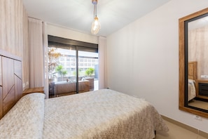 Un dormitorio con una cama grande, un ventanal corredero a un balcón y un espejo en la pared.