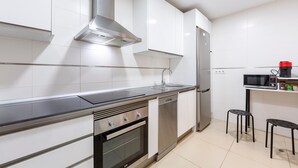 A modern kitchen with stainless steel appliances, white cabinetry, and a microwave on a shelf.