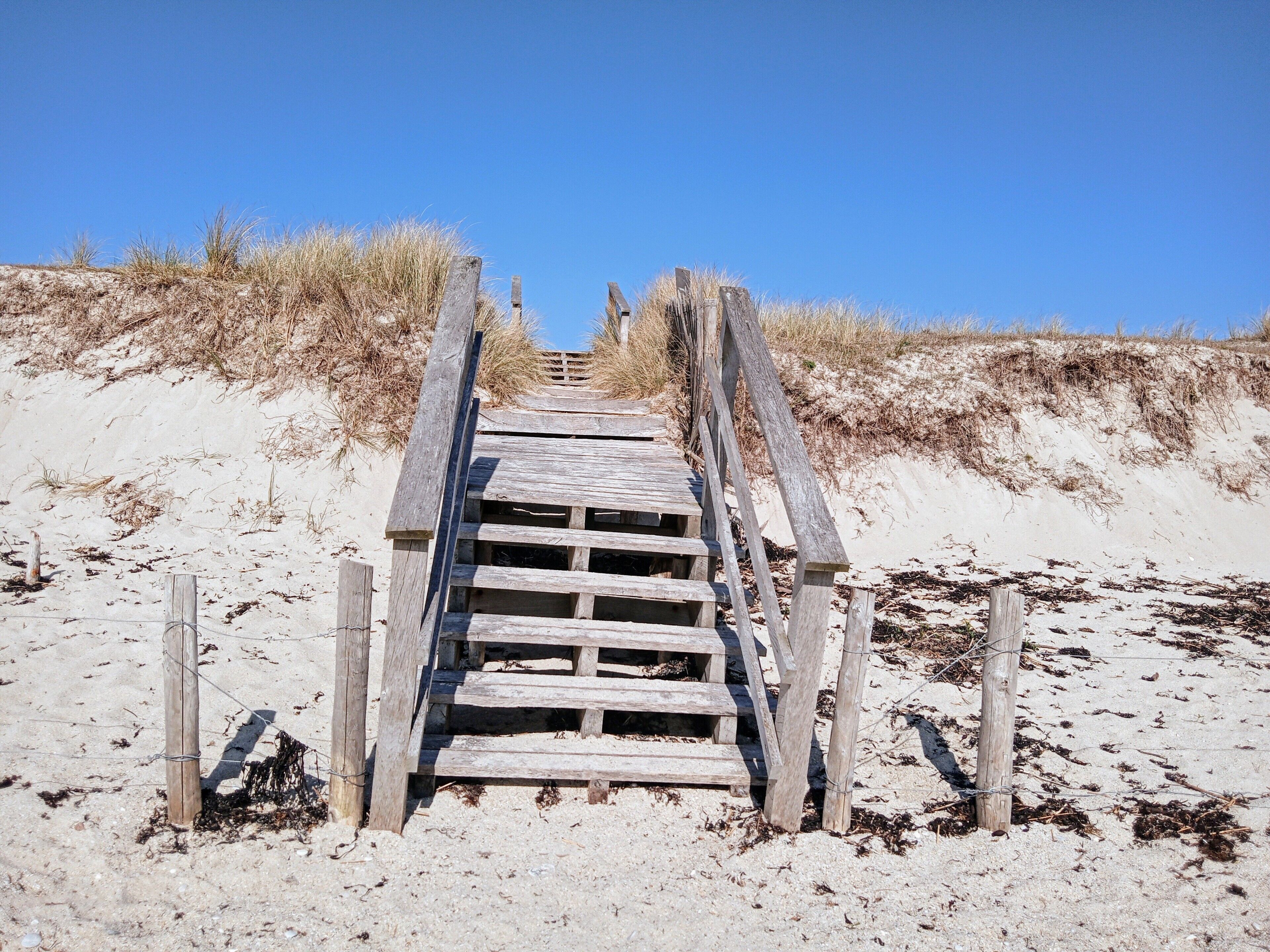 Un escalier en bois menant à une plage de sable, entouré de dunes.