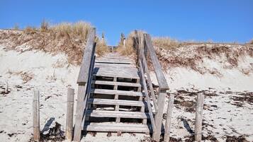 Un escalier en bois menant à une plage de sable, entouré de dunes.