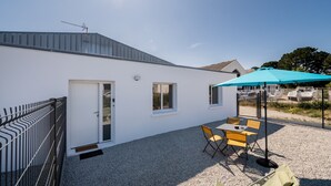 Un edificio blanco con puerta, ventanas y un patio de grava con mesa y sillas.