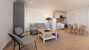 Una sala de estar moderna con un sofá, sillas, una mesa de centro y una cocina al fondo.