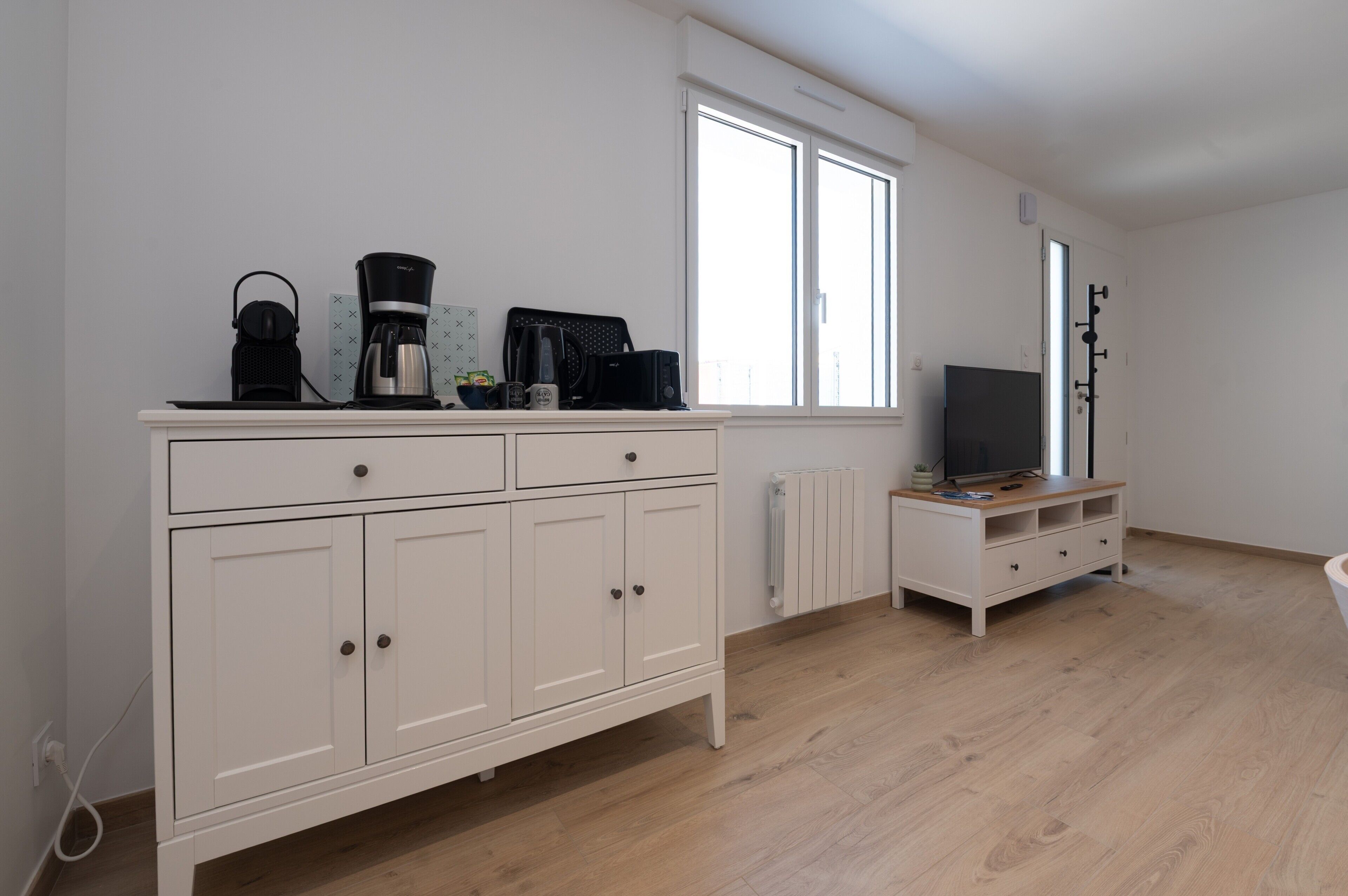 A room with a white cabinet, a radiator, a television, and a window.