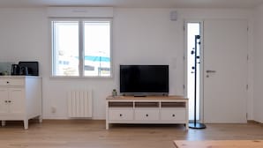 Una habitación con una televisión sobre un mueble de madera, un armario blanco, un radiador y una puerta con espejo.