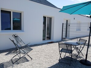 Un patio con una mesa y sillas, una sombrilla azul y un edificio blanco con ventanas.