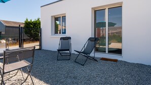 A patio with two chairs and a table, a white building with a window and a door, and a blue umbrella. - Bâbord, quiet artisan area, near port & beach, wifi, parking, towels & cleaning not included (Arzon)